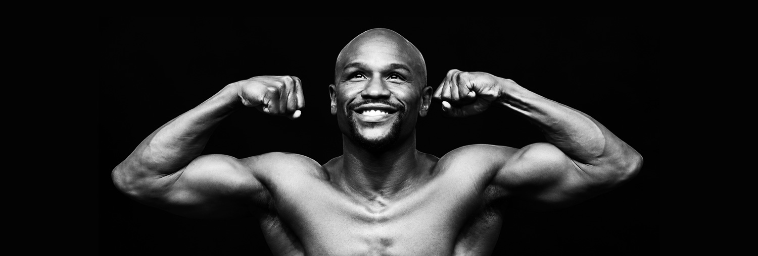 Portrait de Floyd Mayweather sur fond noir, les bras levés.