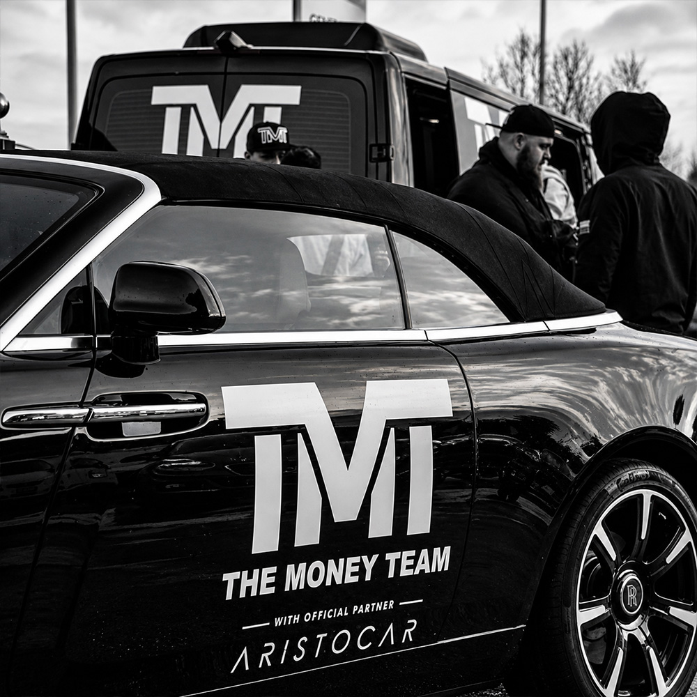 Lettrage blanc TMT et Aristocar sur la Rolls-Royce noire, avec un véhicule de l’équipe à l’arrière-plan.